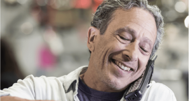 Man smiling while talking on phone Man is holding a phone to his ear with his shoulder and smiling.